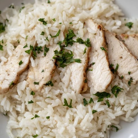 A close-up view of juicy grilled chicken atop fragrant, fluffy rice cooked in savory garlic butter, perfect for a comforting dinner.