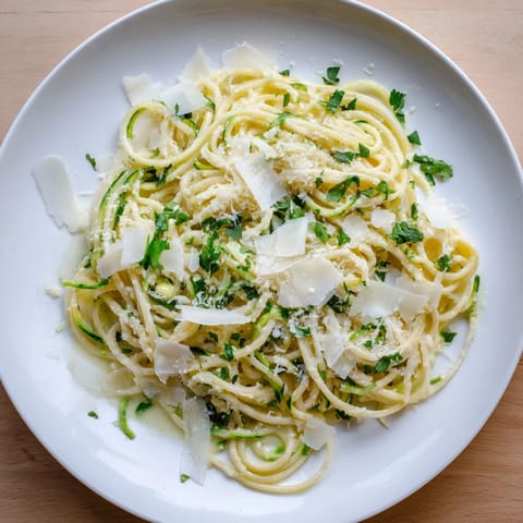 A close-up of freshly made Lemon Zucchini Pasta garnished with chopped parsley and a wedge of lemon.