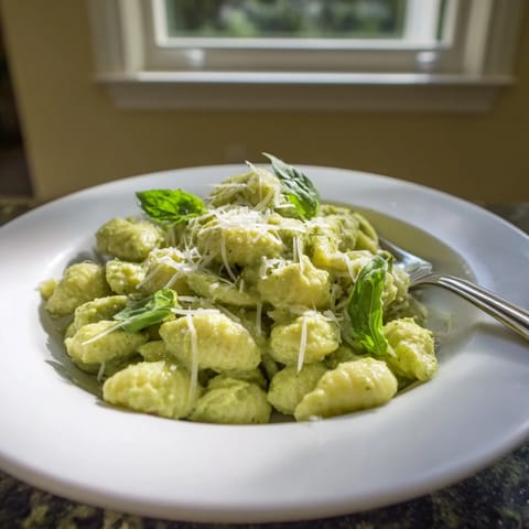 Freshly tossed creamy avocado pesto mac with al dente macaroni, vibrant green sauce, and a sprinkle of cracked black pepper on top.  