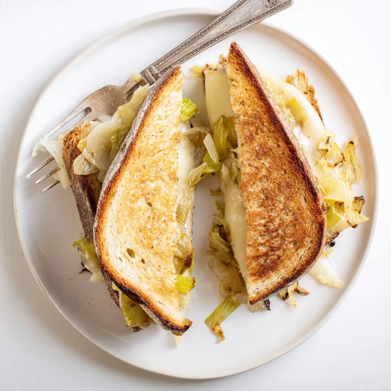 A freshly grilled Havarti & Caramelized Leek Grilled Cheese sandwich, featuring buttery sourdough bread and melted cheese on a rustic wooden table.