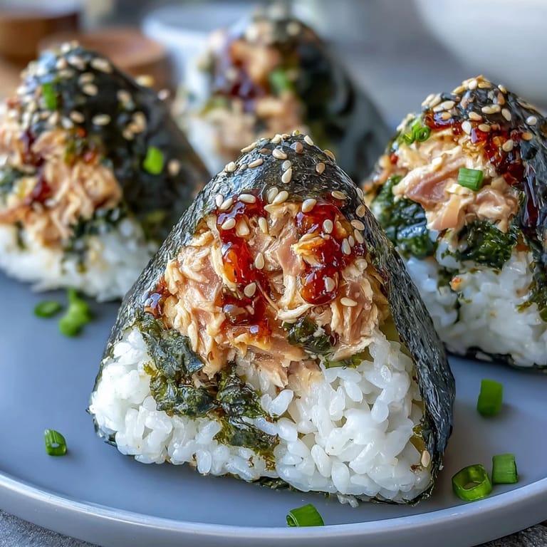 Golden-brown nori-wrapped onigiri with spicy tuna filling, garnished with sesame seeds and green onions.