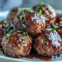 Glossy Slow Cooker Peach Glazed Meatballs simmer in a sweet, tangy sauce, garnished with fresh parsley for a party appetizer.
