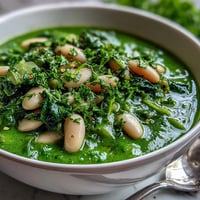 A vibrant green bowl of spinach and white bean shamrock soup, garnished with fresh chives and served steaming hot.