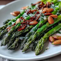 Lemon butter asparagus with almonds in a white serving bowl, garnished with parsley and toasted nuts.  